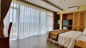Une chambre d’hôtel avec un grand lit, une télévision, des meubles en bois et une vue à travers des rideaux transparents.