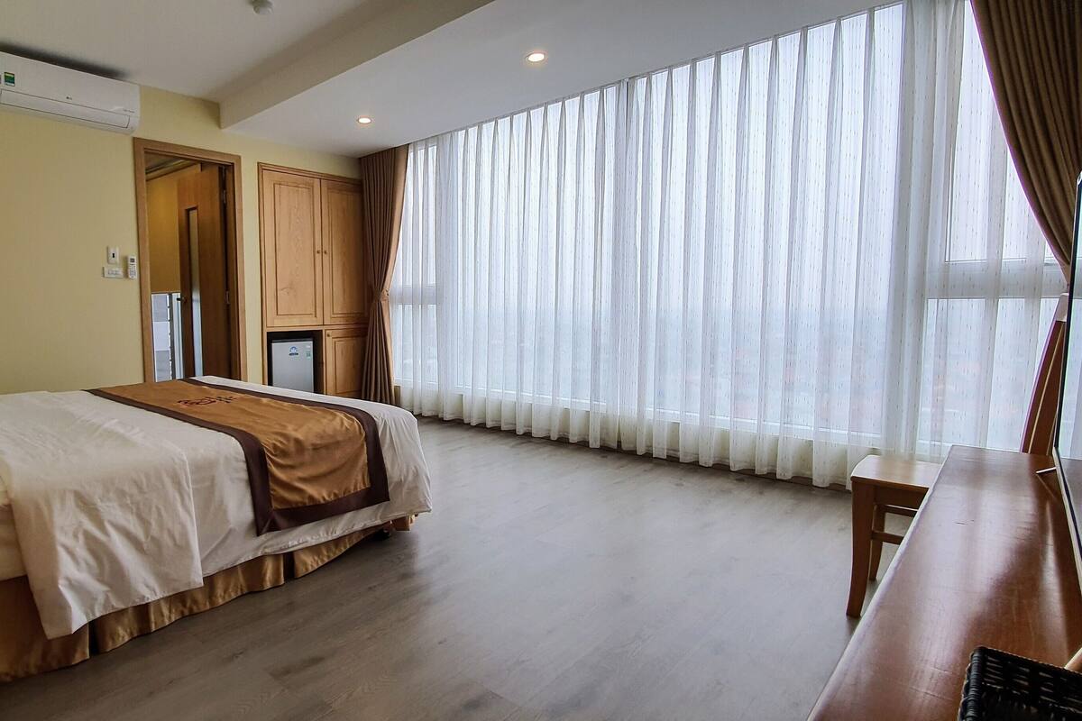 A hotel room with a bed, bedside table, and a large window with curtains.