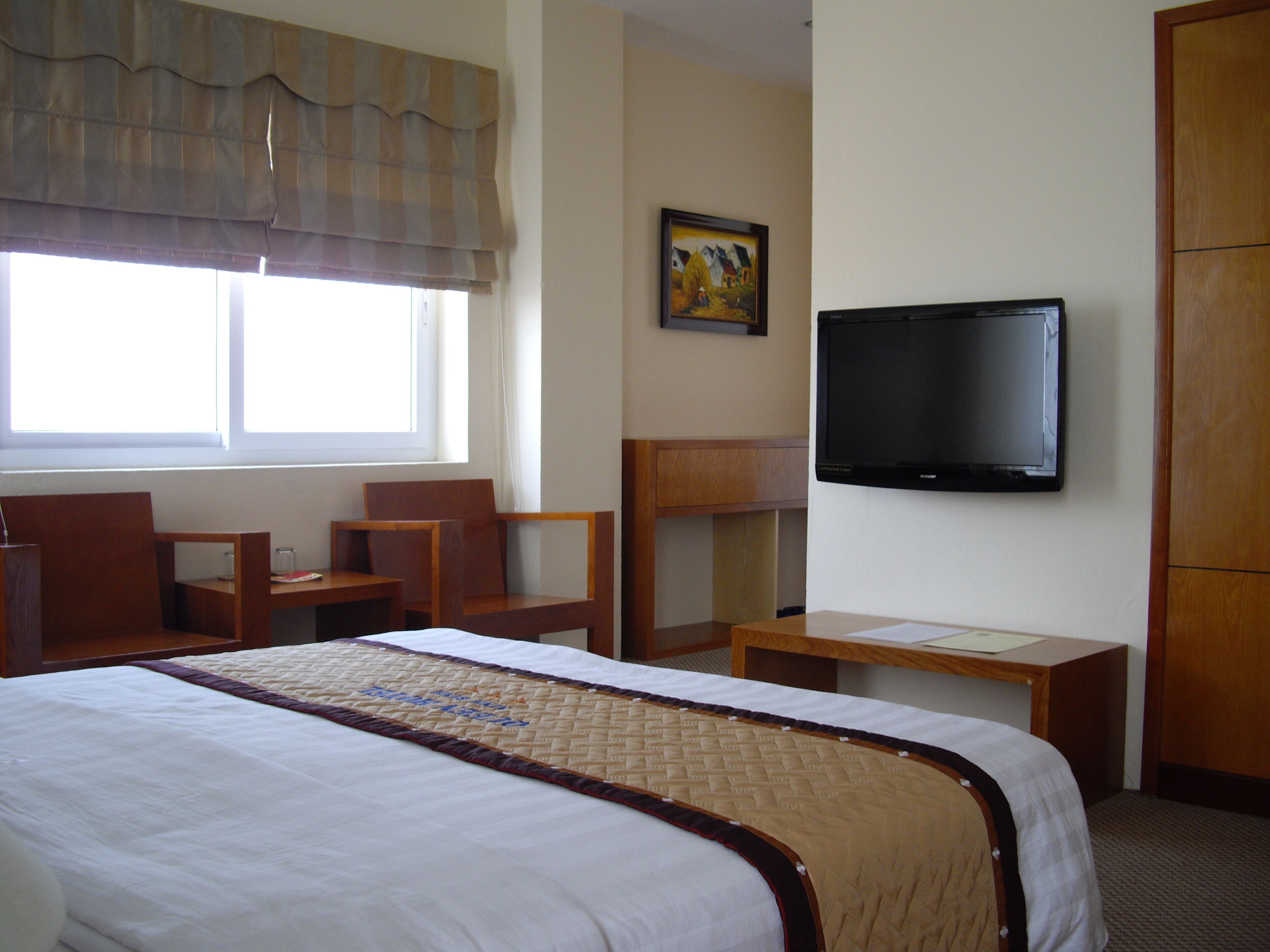 A hotel room with a bed, a desk, a chair, a television, and a window with curtains.