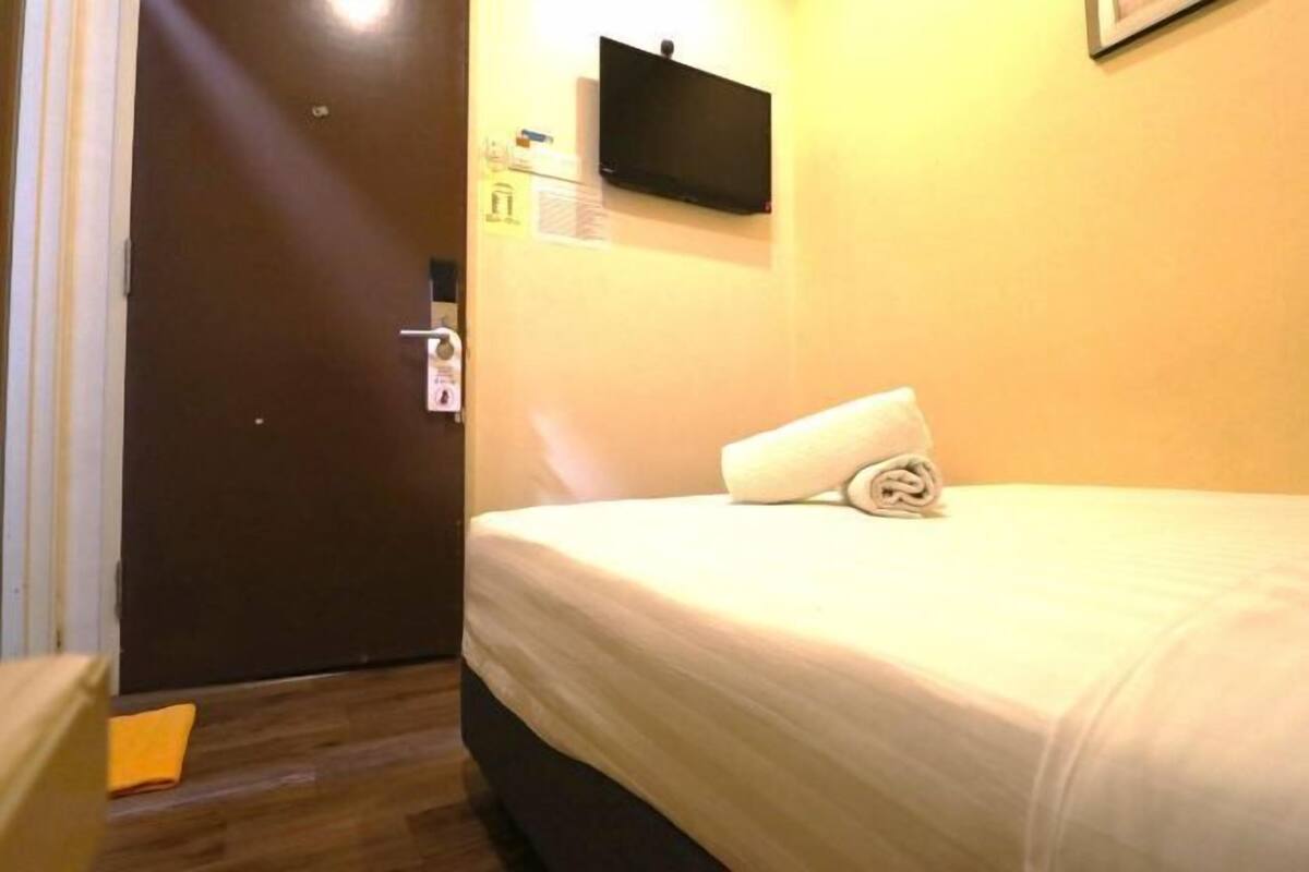 A hotel room with a bed, a flat-screen TV mounted on the wall, a door, and a wooden floor.