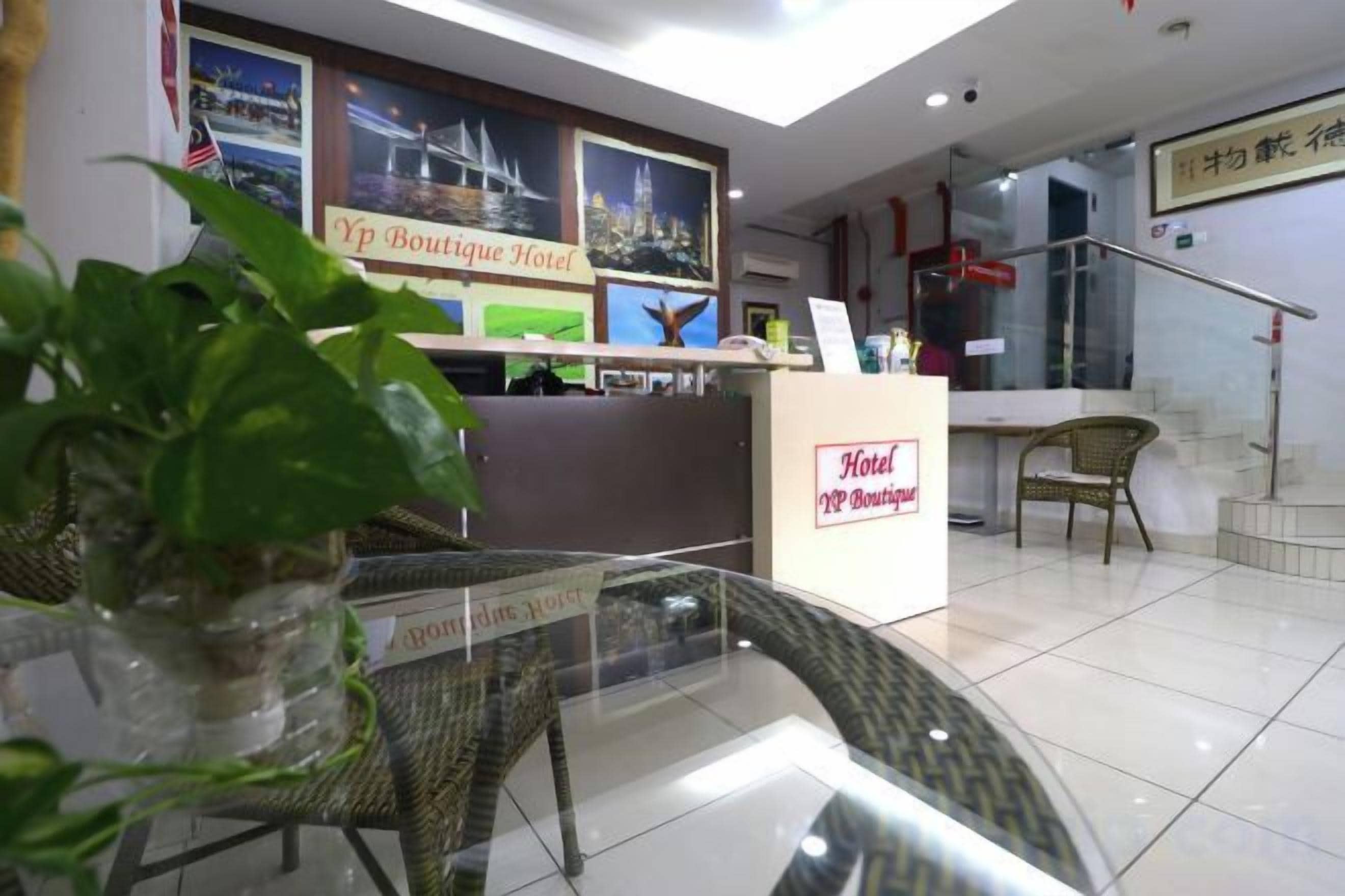 Un espace d’accueil d’hôtel comprenant un comptoir de réception, une plante en pot, des chaises en osier et un panneau indiquant le nom de l’hôtel.