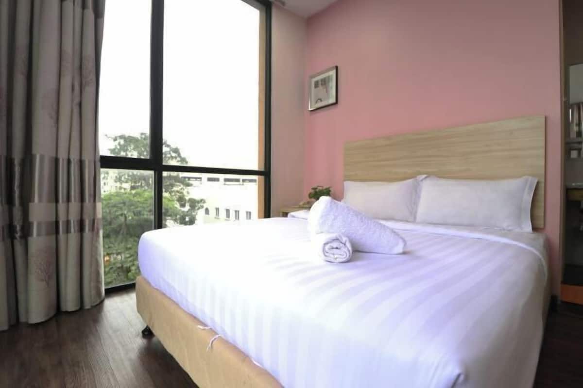 A hotel room with a large bed, a wooden headboard, and a view of greenery outside.