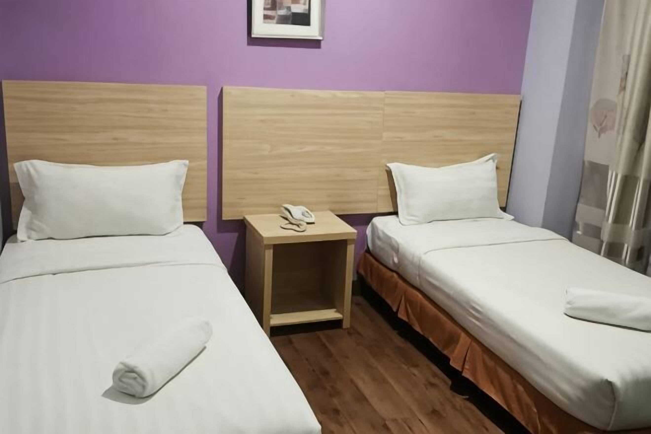 Two single beds with wooden headboards, a nightstand with a phone, and a purple wall.