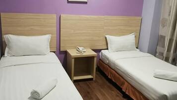 Two single beds with wooden headboards, a nightstand with a phone, and a purple wall.