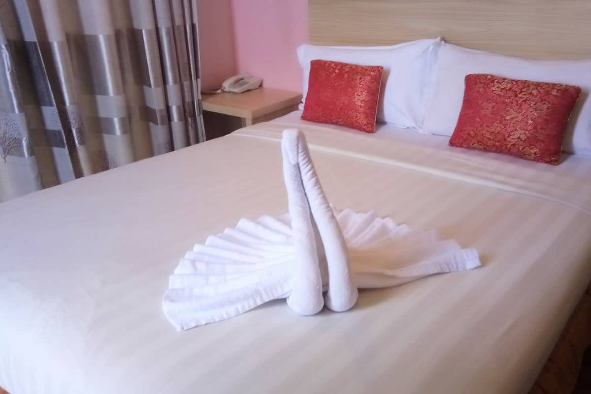 A neatly made bed with white linens and two red pillows, a bedside table with a phone, and a curtain partially drawn to the side.