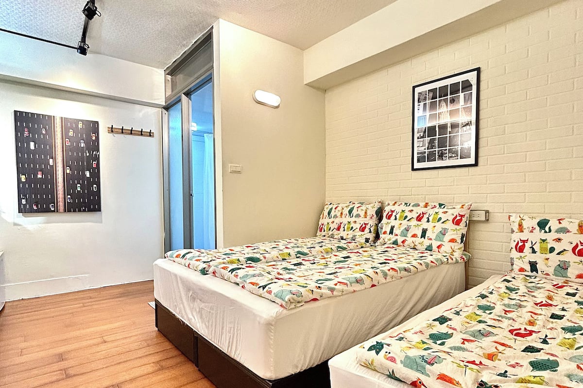 A bedroom with two beds, wooden flooring, a white brick wall, and a ceiling light fixture.
