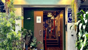 A hotel entrance with a green artificial grass mat, a blue bench, and potted plants. - Ximen Triple Tiger Hostel (Taipei)