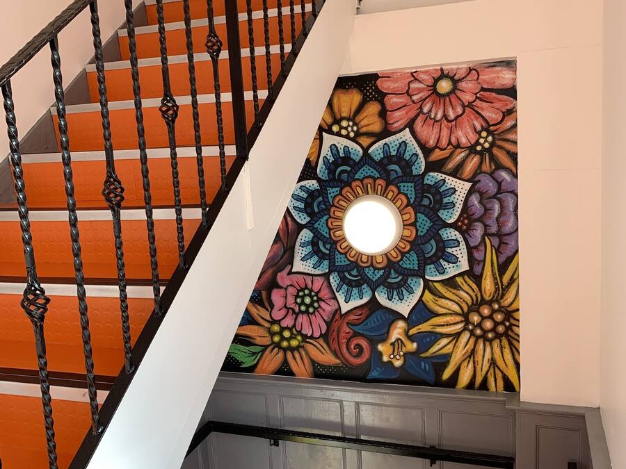 Eine Treppe mit schwarzer Metallgeländer und einer farbenfrohen Blumenmalerei an der Wand.