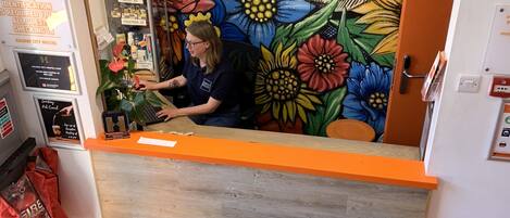 A reception area with a colorful mural, a reception desk, and a sign indicating the location as Galway City Hostel, Eyre Square.