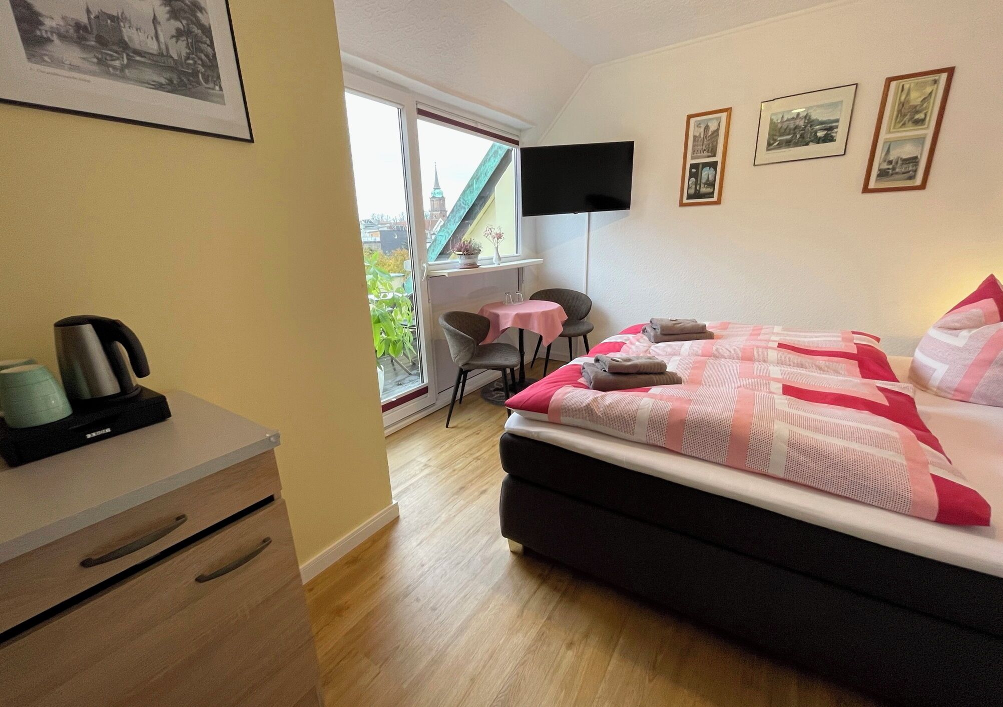 A bedroom with a bed, a desk, a chair, a TV, and a window with a view of a building.