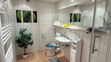 Een moderne badkamer met witte tegels, een toilet, een wastafel, een douche en een kamerplant.
