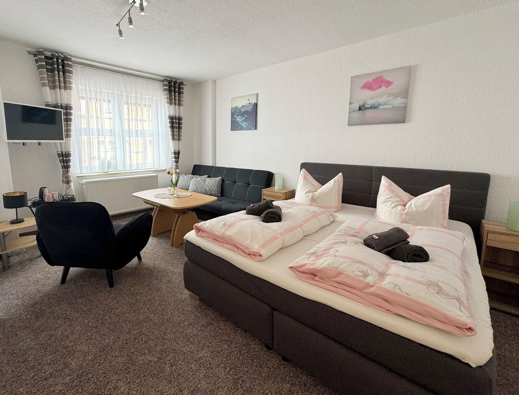 Ein Schlafzimmer mit Bett, Schreibtisch, Stuhl, Fernseher und einem Fenster mit Vorhängen.
