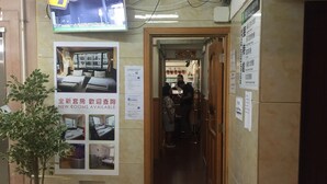 A hotel reception area with a television displaying a room layout, a poster advertising new rooms, and a potted plant. - Traveller Friendship Hostel (Kowloon)