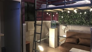 A compact room with a bunk bed, a small desk, a couch, a ladder, a water dispenser, and a wall-mounted phone. - Traveller Friendship Hostel (Kowloon)