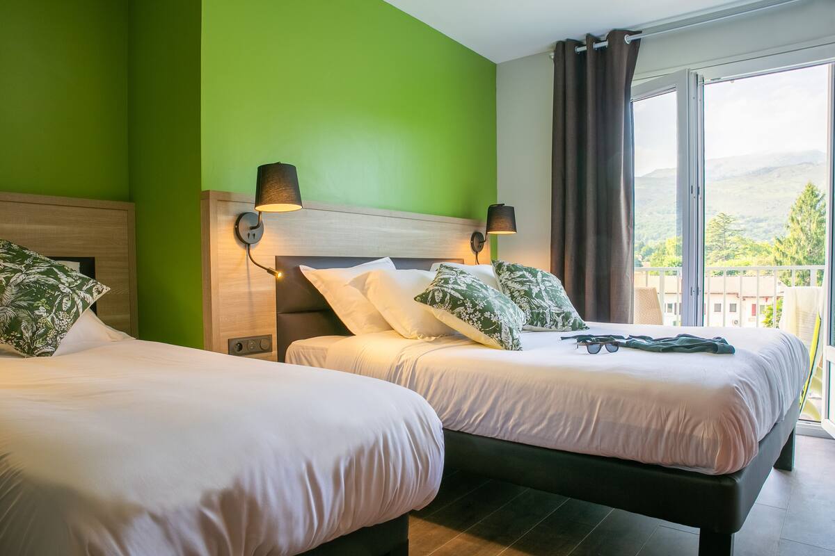 A hotel room with two beds, green walls, and a view of a mountainous landscape.