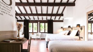 A hotel room with two beds, a desk with a chair, a vase with dried flowers, and large windows with curtains. - Hôtel du Pont d'Ascain (Ascain)