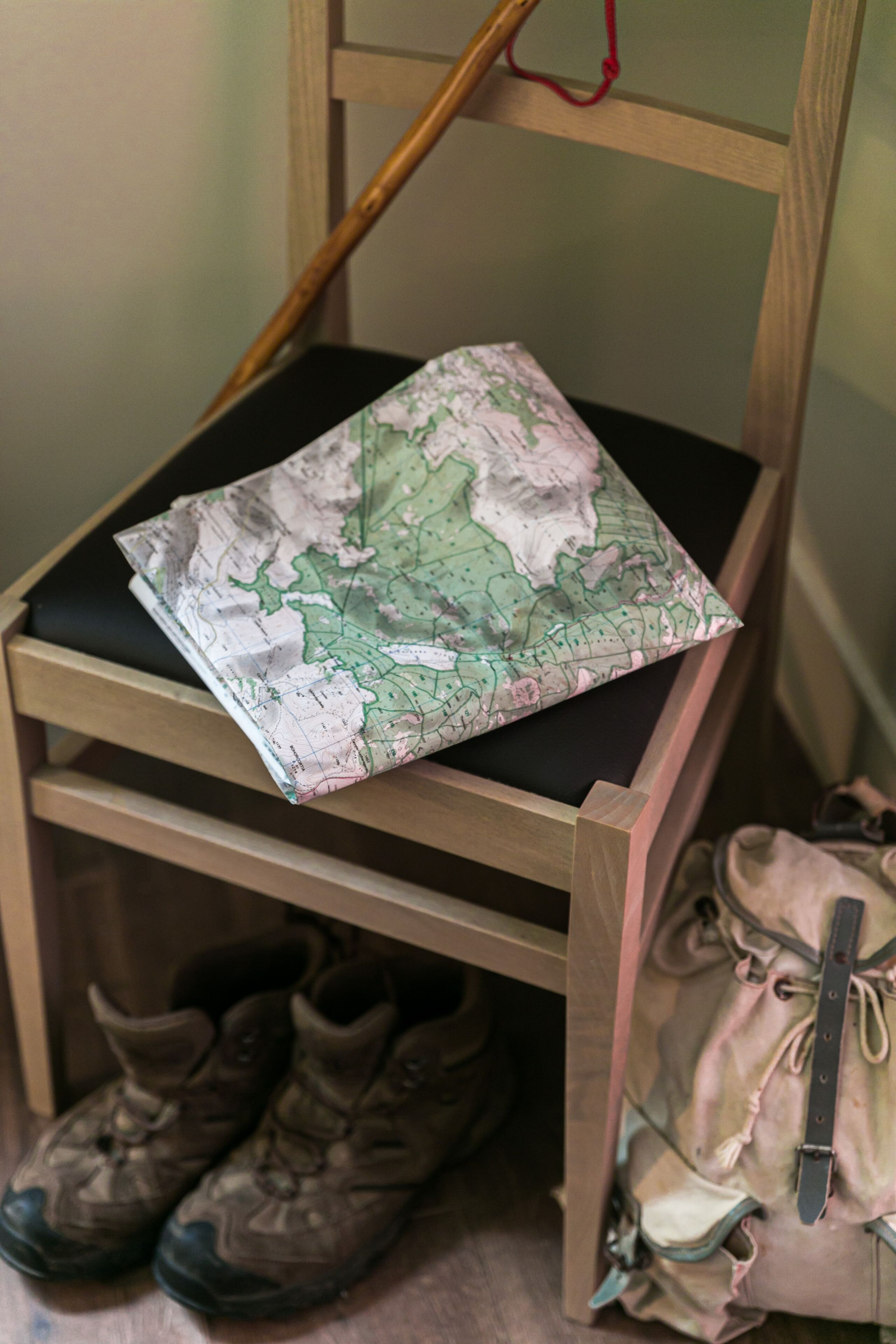 Una silla de madera con un cojín con mapa, un par de botas y una mochila en el suelo.