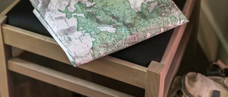 Una silla de madera con un cojín con mapa, un par de botas y una mochila en el suelo.