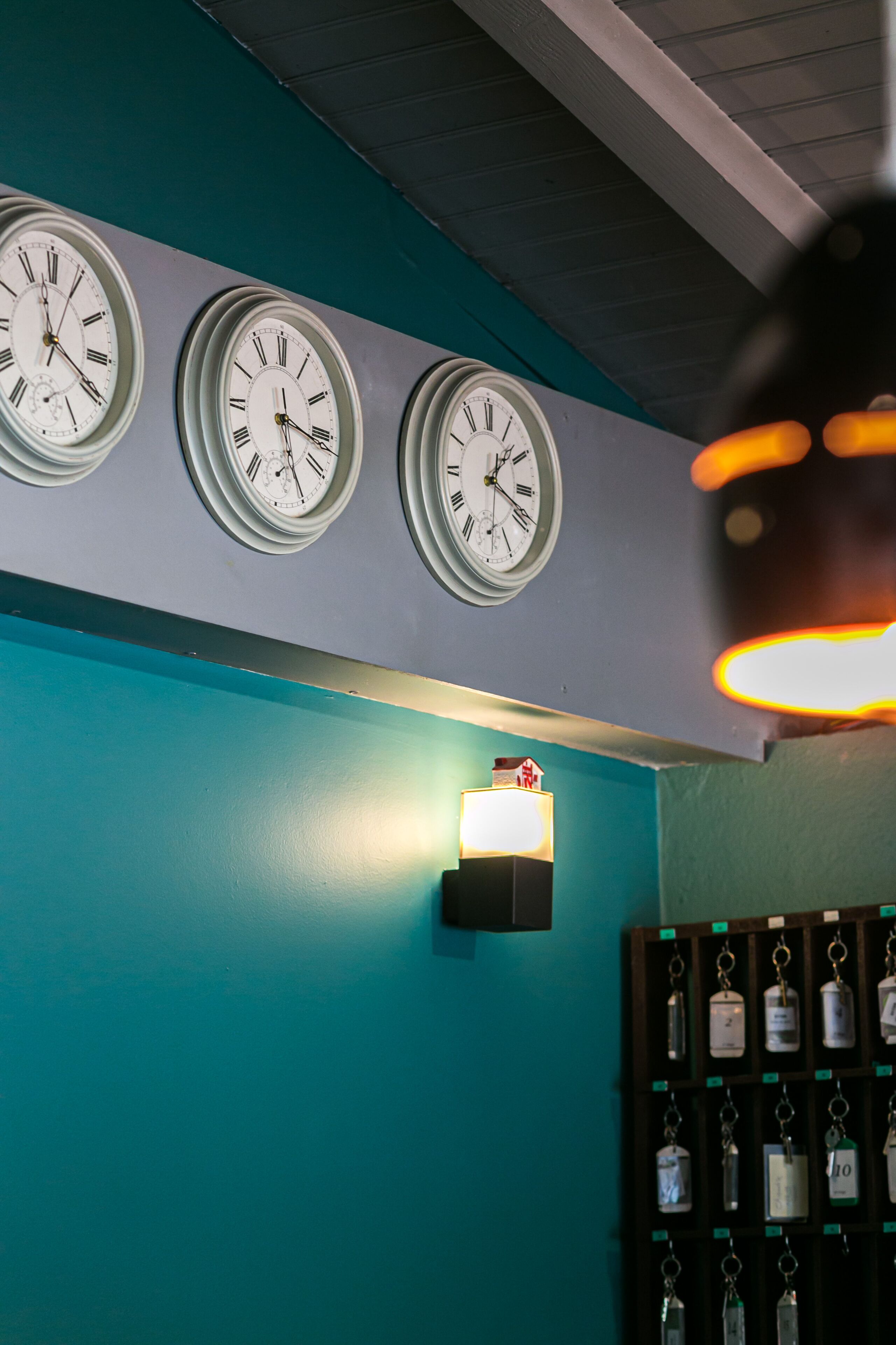 A wall with three clocks and a wall-mounted light fixture.