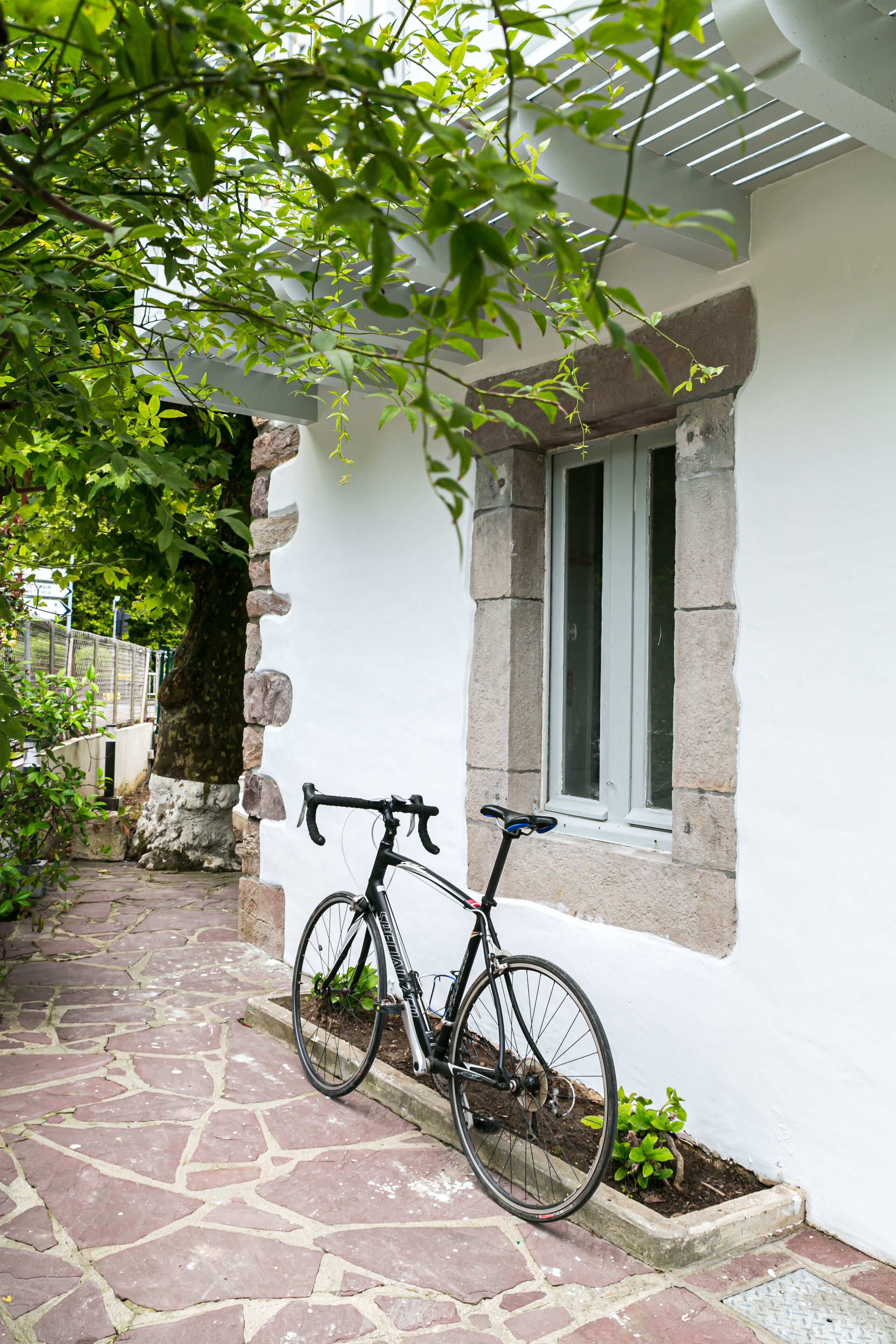 A bicycle leaning against a stone wall near a window with a view of a stone pathway and greenery.