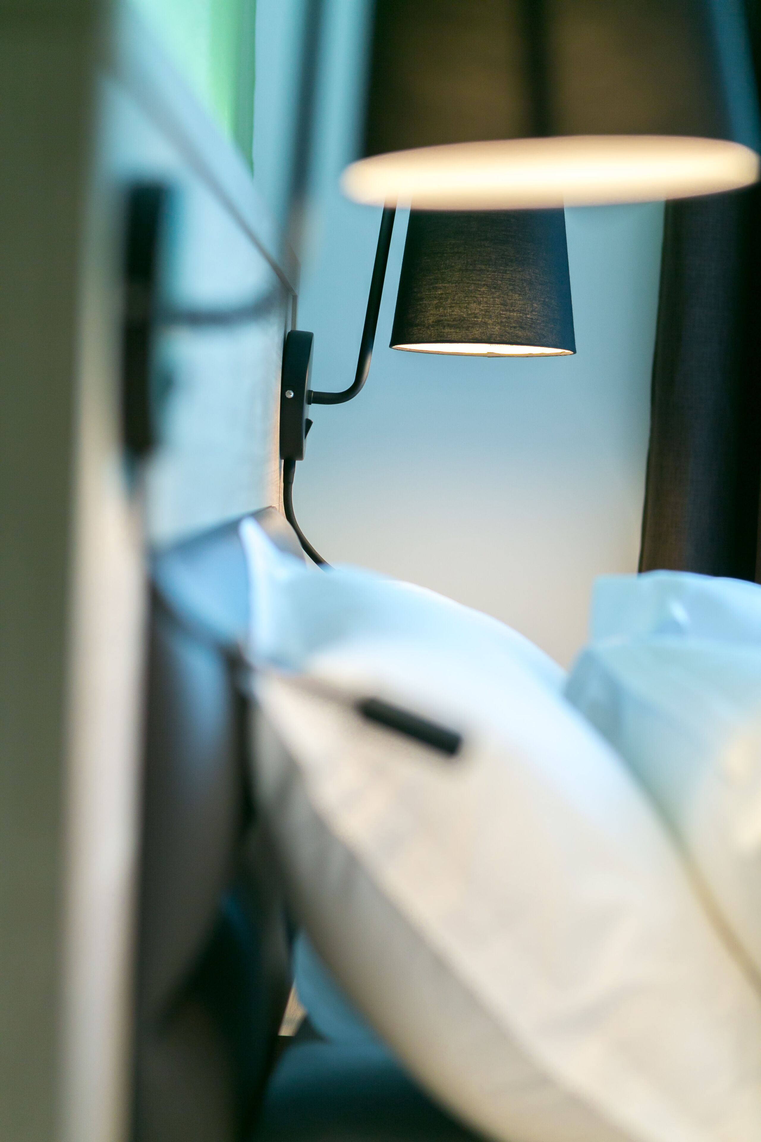 Ein Detailbild eines Bettes mit einer Lampe daneben, einem Kopfkissen und einer Decke.