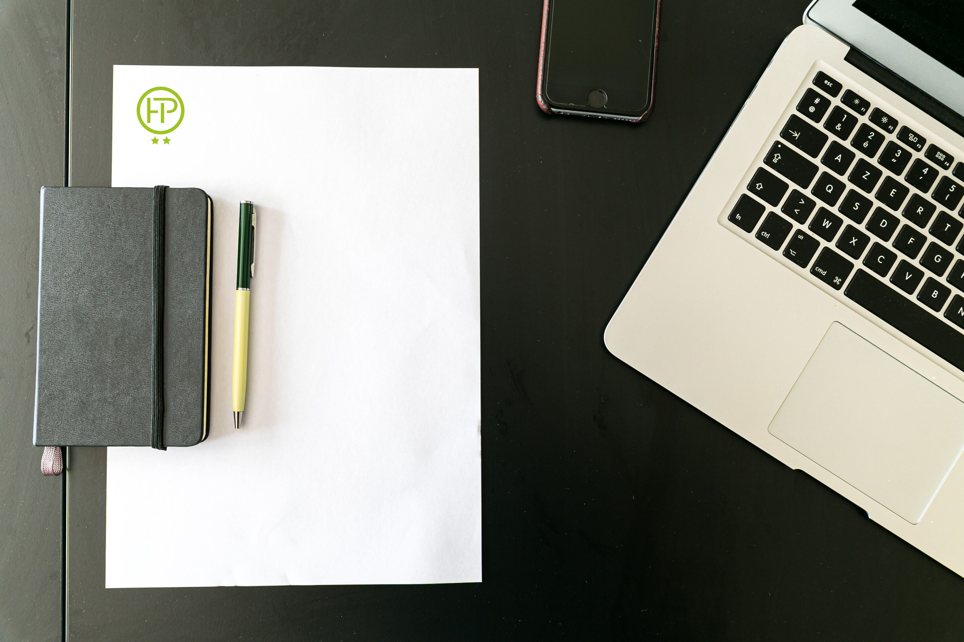 Una computadora portátil, un teléfono inteligente, un cuaderno y un bolígrafo sobre una superficie oscura.