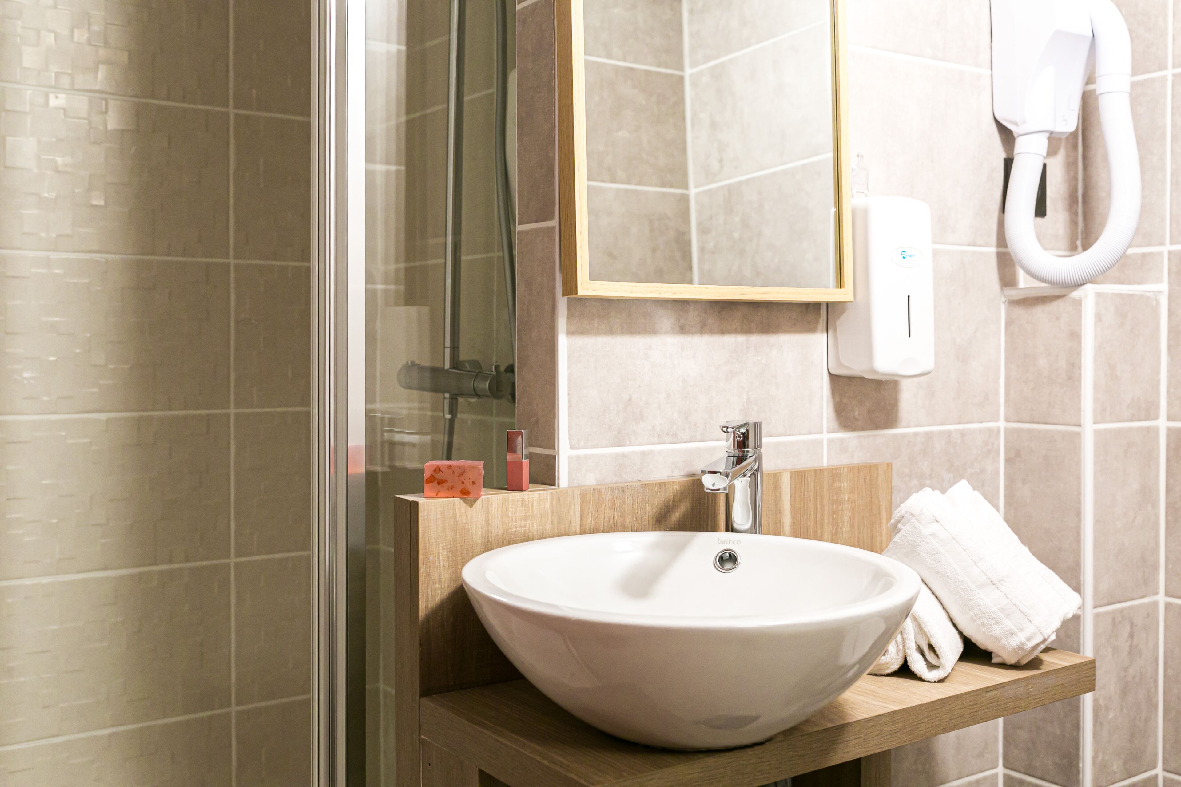 A bathroom with a large white sink, a glass shower enclosure, a wooden vanity, and a towel rack.