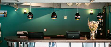 Un área de recepción con mostrador de madera oscura, paredes color verde azulado e iluminación colgante.