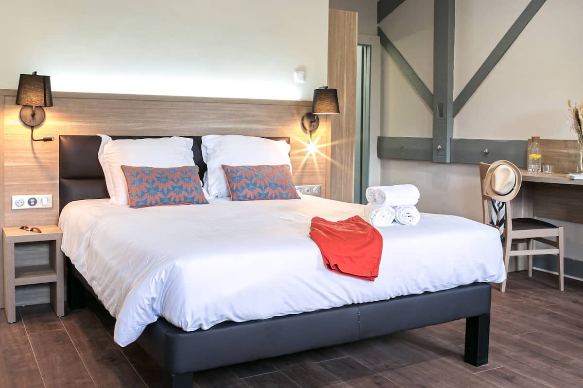 A modern hotel room with a large bed, bedside lamps, a desk, and an air conditioning unit.