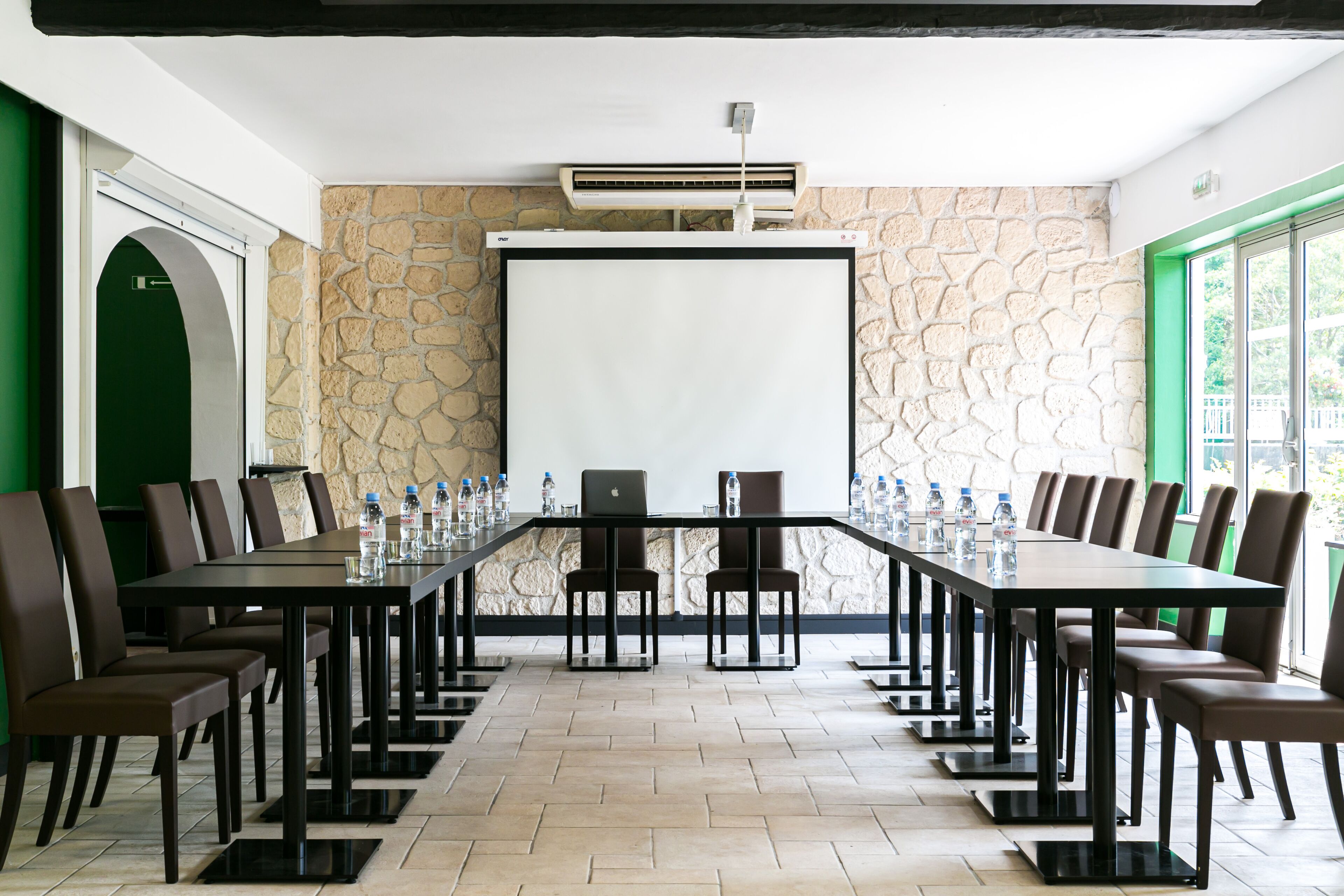 A conference room with a long table, chairs, a projector screen, and an air conditioning unit.