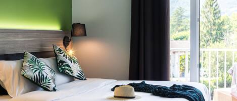A hotel room with a bed, a hat, and a view of greenery outside.
