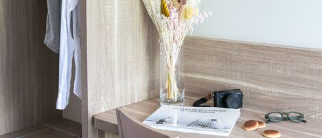 Une chaise en bois, un vase en verre contenant des fleurs séchées, un appareil photo, une paire de lunettes et un magazine sur une table en bois.