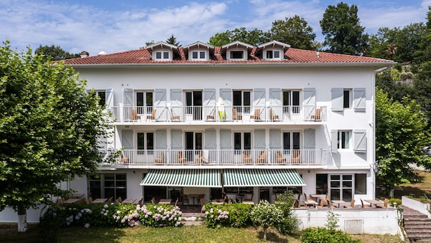 A two-story hotel with a white facade, multiple balconies with outdoor seating, and a green awning over the entrance. - Hôtel du Pont d'Ascain (Ascain)