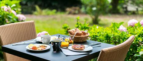 Una mesa colocada al aire libre con alimentos para el desayuno, como cruasanes, fruta y una taza de café.