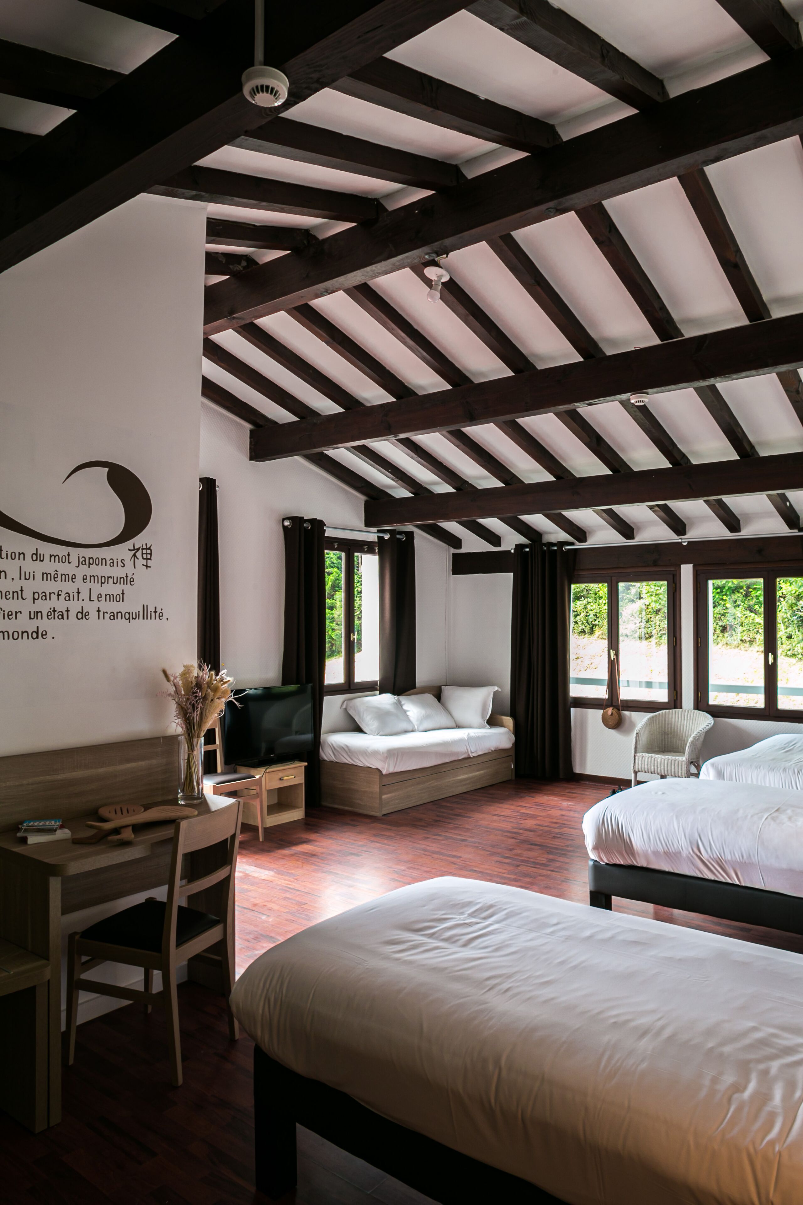 A room with wooden beams, a bed, a desk, and a chair.