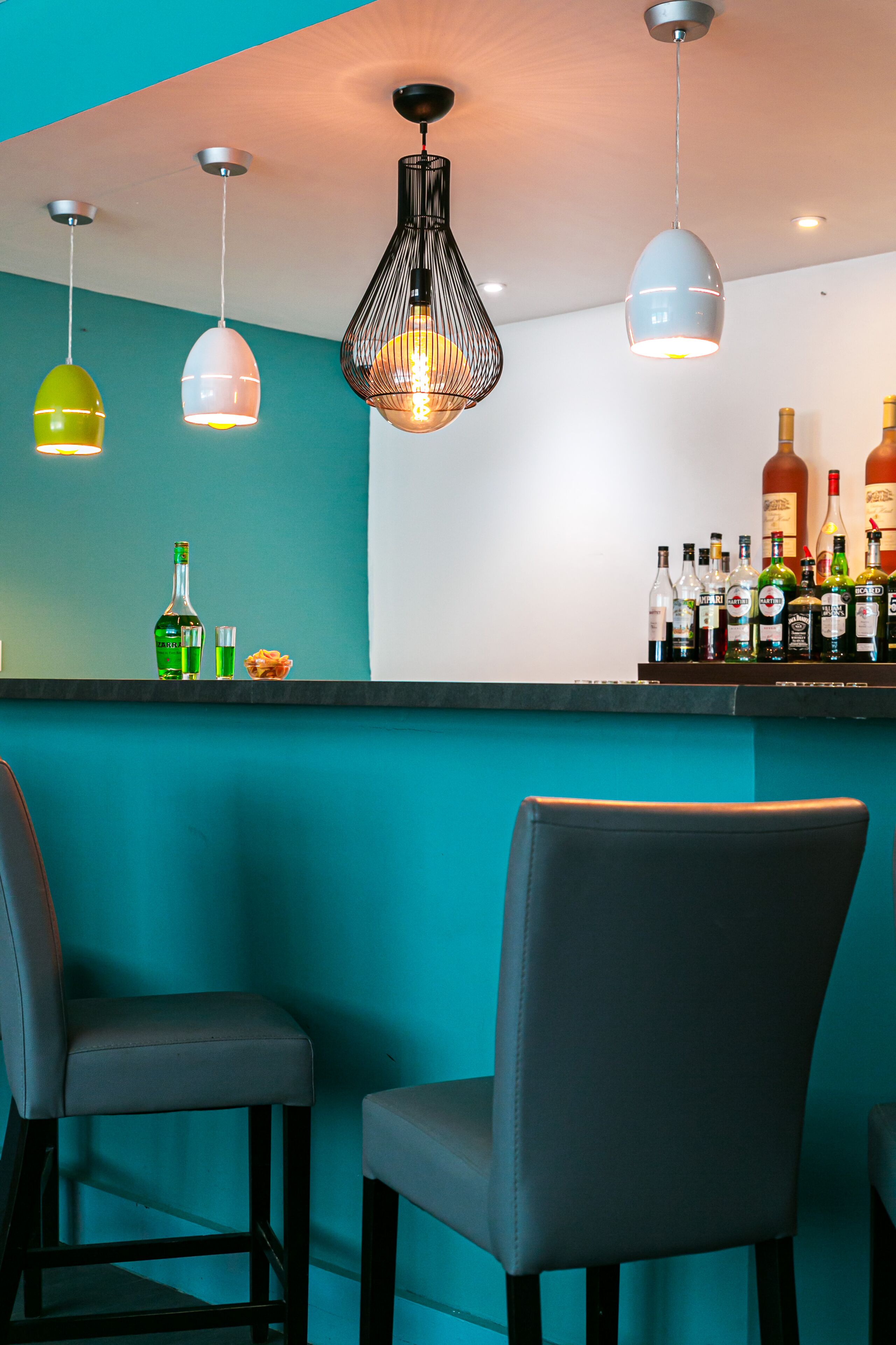 A bar area with teal walls, three pendant lights, and a bar stocked with liquor bottles.