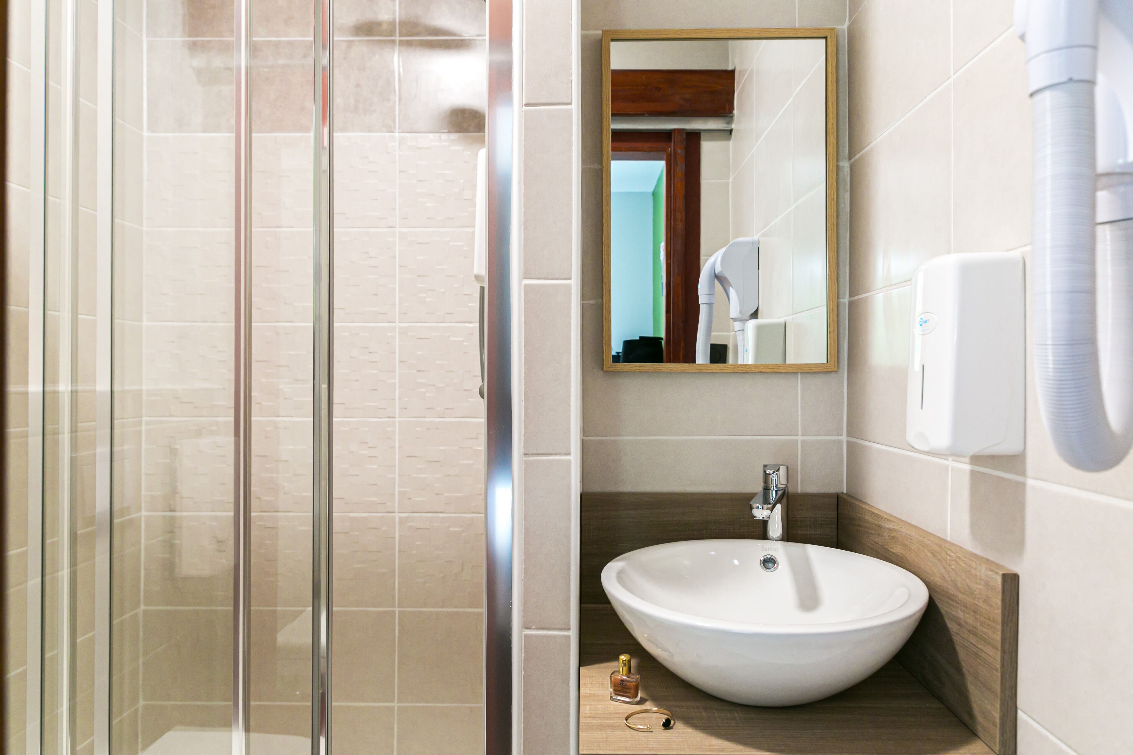 Un baño moderno con cabina de ducha de vidrio, un lavabo blanco con encimera de madera y un espejo sobre el lavabo.