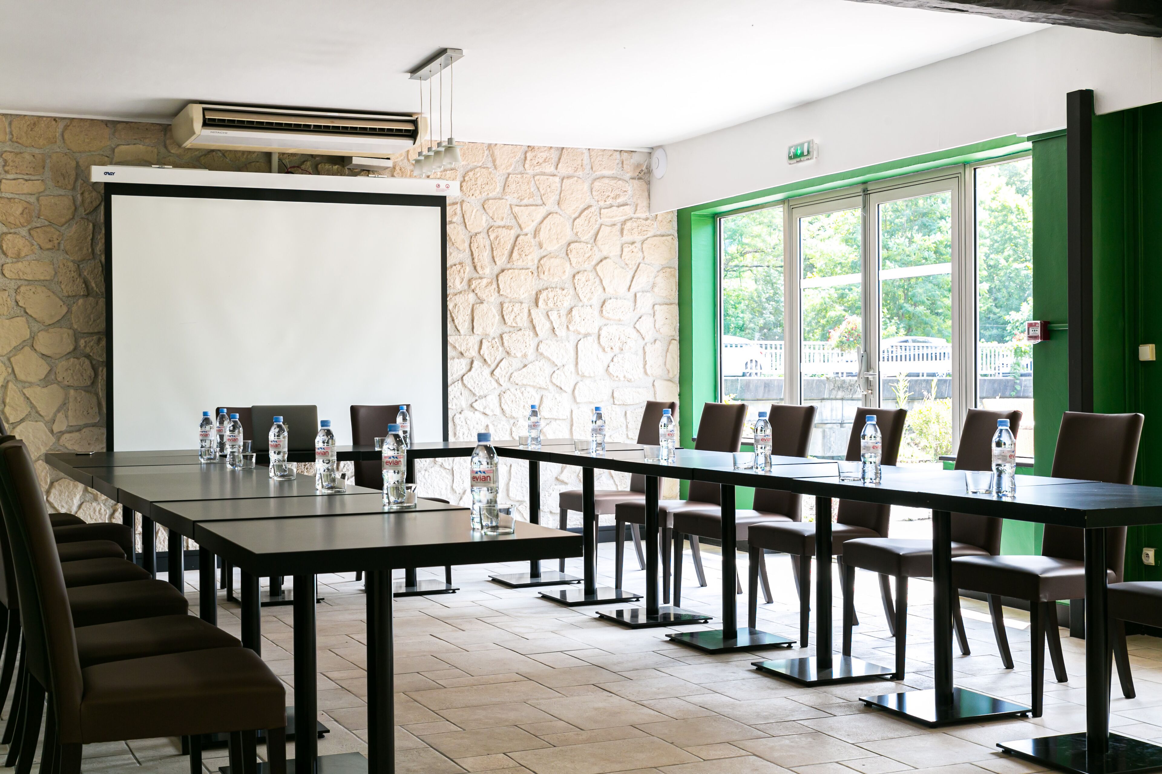 Un salón de conferencias con una larga mesa, sillas, una pantalla de proyector y una pared de piedra.