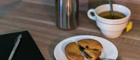 A wooden table with a notebook, a thermos, a mug with a spoon, and a plate with cookies.