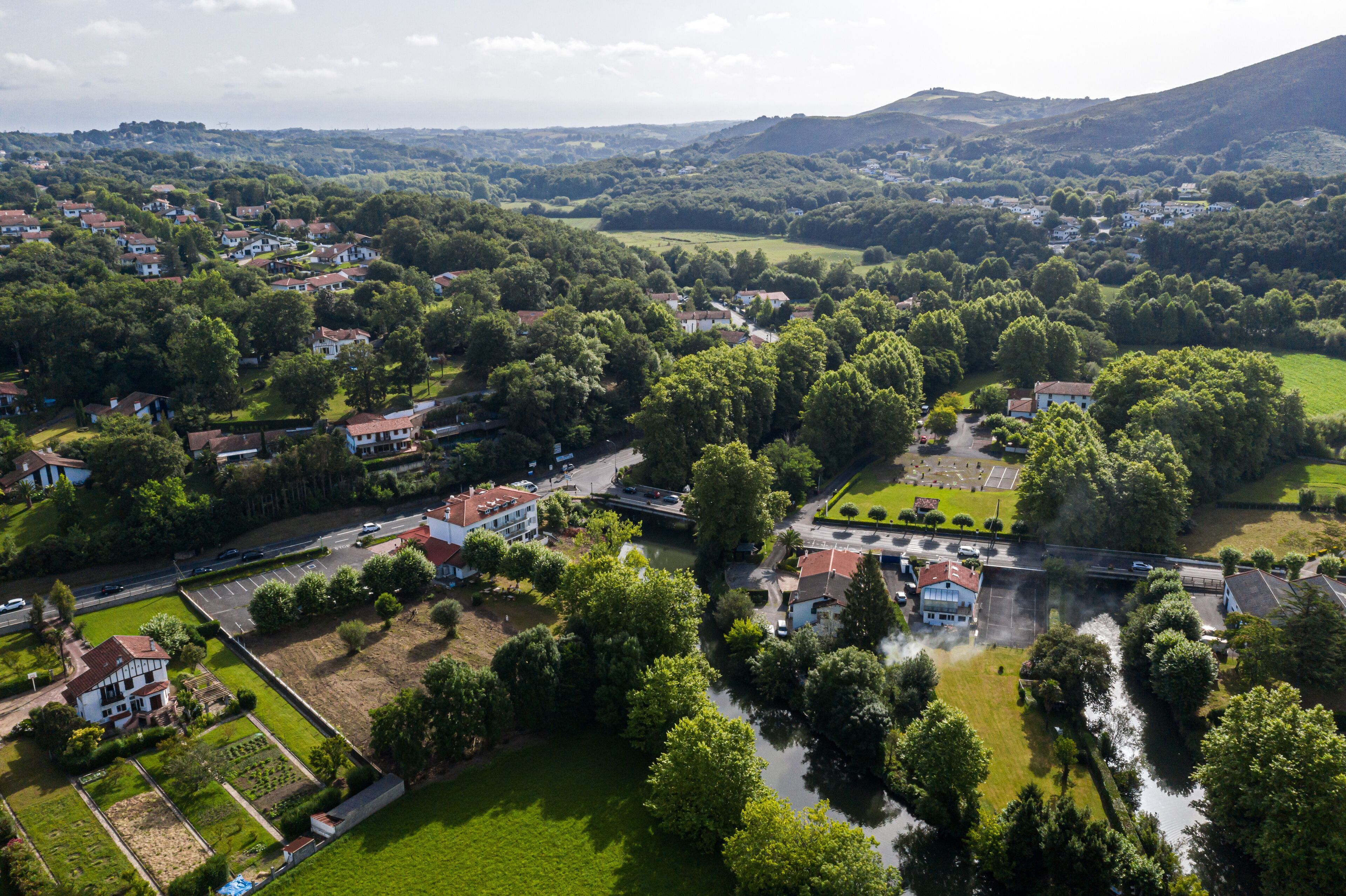 An aerial view of a residential area with houses, a river, and surrounding greenery.