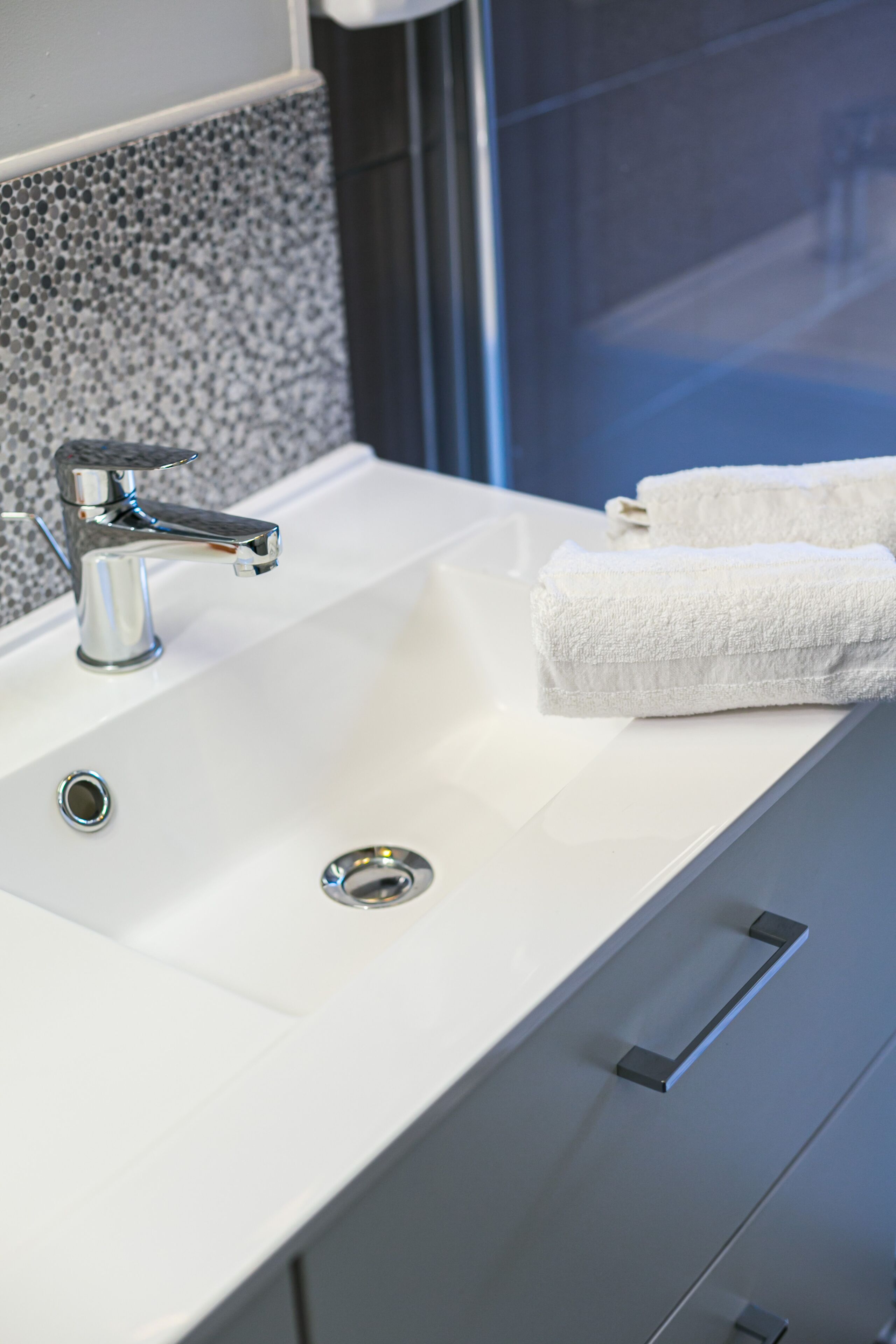 A modern bathroom sink with a chrome faucet, a white towel, and a textured wall backsplash.