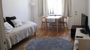 A small, well-lit room with a bed, a desk with a chair, a television, and a window with curtains. - Helsinki Apartment (Helsinki)