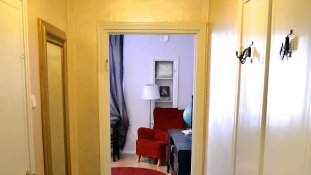 A narrow hallway with a dark floor leading to a room with a red chair and a lamp. - Helsinki Apartment (Helsinki)
