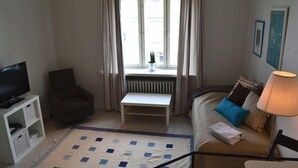 A compact living room with a sofa, a television, a small table, and a window with curtains. - Helsinki Apartment (Helsinki)