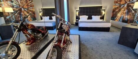 Habitación de hotel con dos camas, una motocicleta y un mural de paisaje urbano en las paredes.