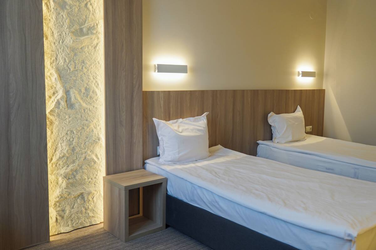 A hotel room with two beds, a nightstand, and a textured wall.