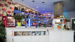 A bar area with shelves of bottles, a refrigerated display case, and a potted plant. - AQUA Hotel (Varna)