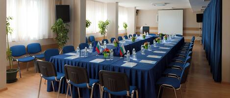 Un salón de conferencias con una larga mesa, sillas azules y banderas.