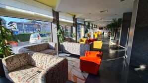 A modern lobby with patterned sofas, a bright orange chair, and a glass wall offering a view of the street. - AQUA Hotel (Varna)