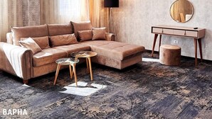 A modern living room with a sectional sofa, a round coffee table, a side table, a floor lamp, a mirror, and a patterned rug. - AQUA Hotel (Varna)